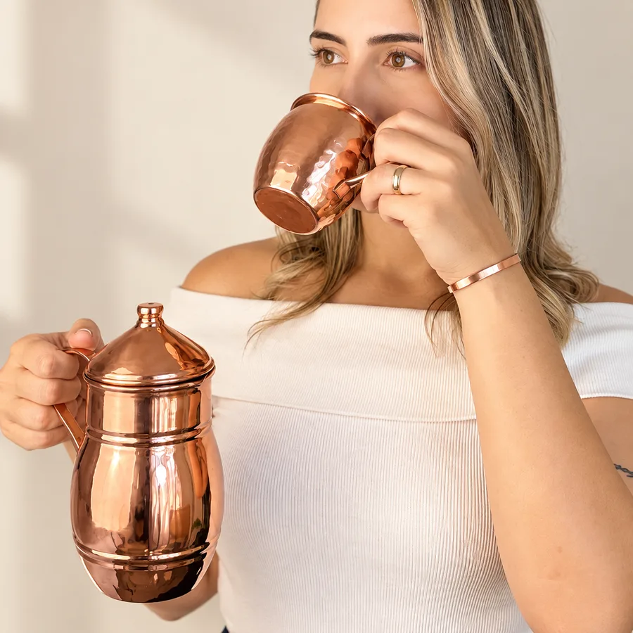 Mulher bebendo água na caneca de cobre